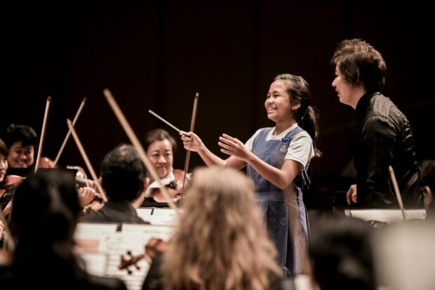A young audience member tries her hand at conducting at the “SSO in Your Community” concert, Agape Auditorium, Paya Lebar Methodist Girls’ School. (Photo Credit: Chrisppics+)
